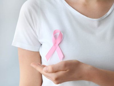 Woman with pink ribbon on light background, closeup. Breast cancer awareness concept